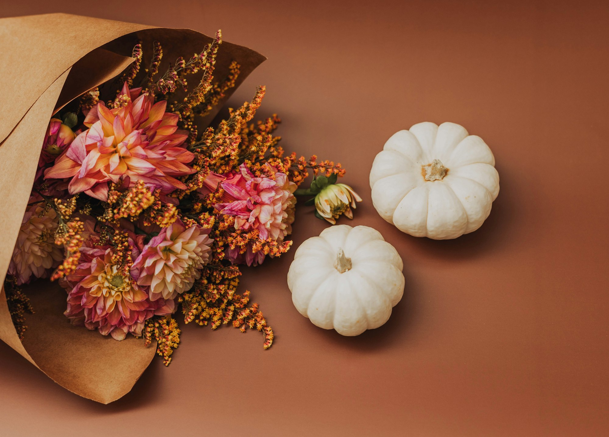 Autumn dahlias wrapped in brown kraft paper beside two small white pumpkins