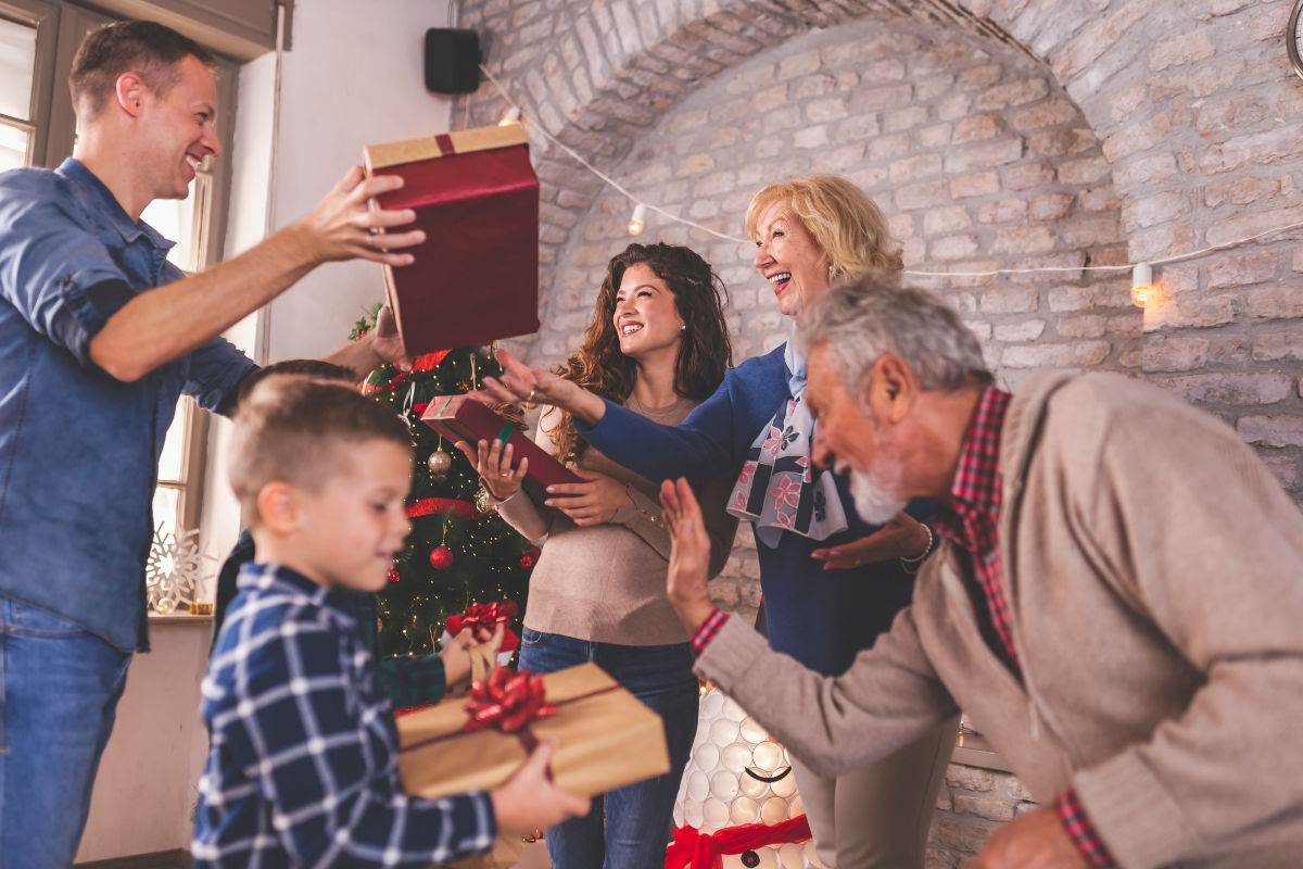 A family swapping wrapped presents in front of a Christmas tree, a boy holding a gift tied with a red bow