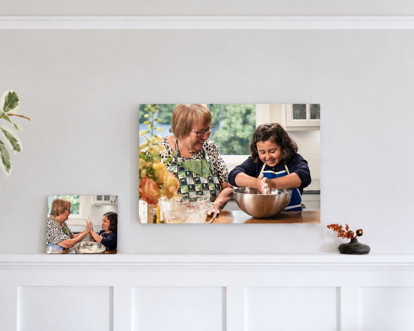 Two family canvas prints of a grandmother and granddaughter baking, hanging above a white mantel