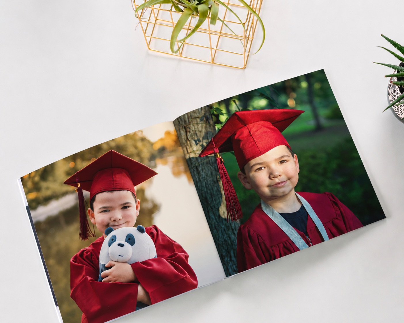 A graduation photo book open to two photos of a young child in a red cap and gown
