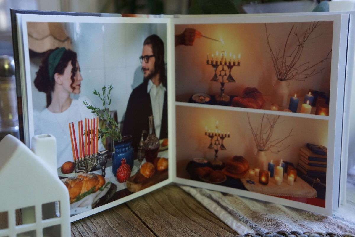 An open photo book with Hanukkah photos, a couple at a holiday table on one page and candles being lit on a menorah on the other