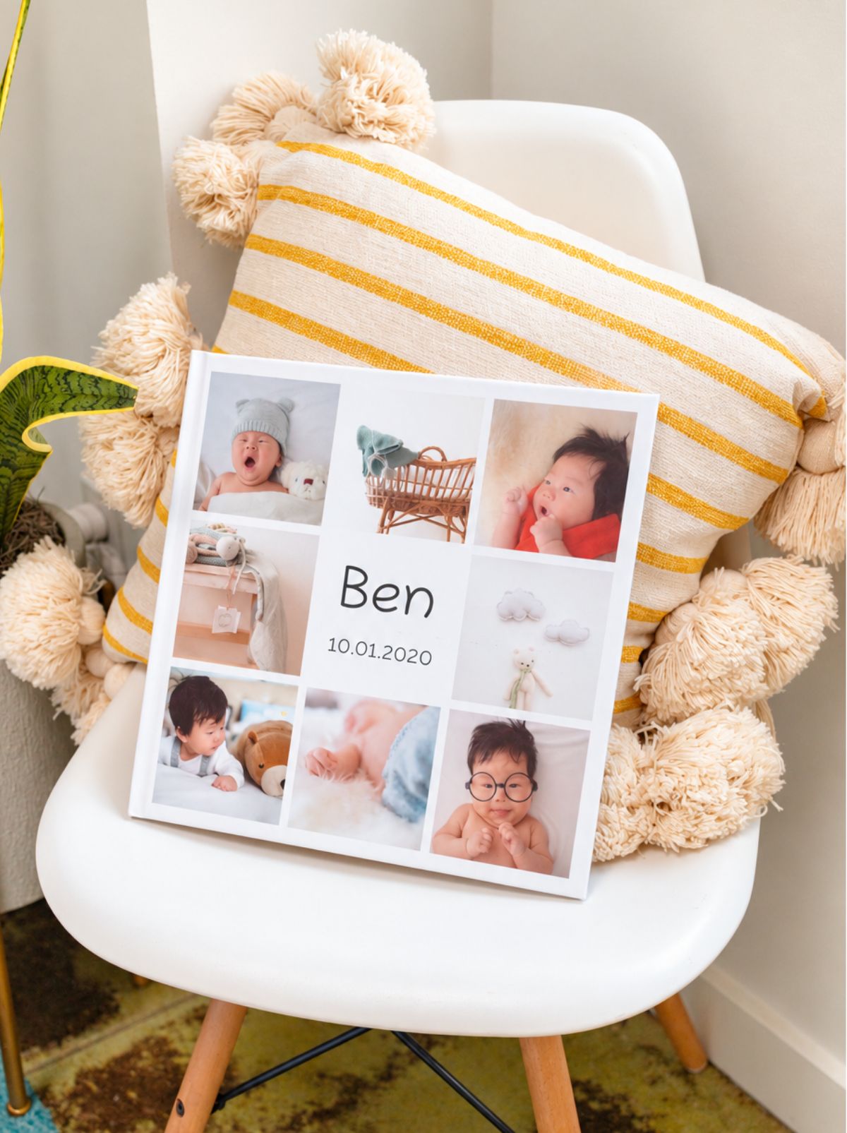 A hardcover baby photo book titled Ben, with a grid of newborn photos, resting on a pillow on a white chair