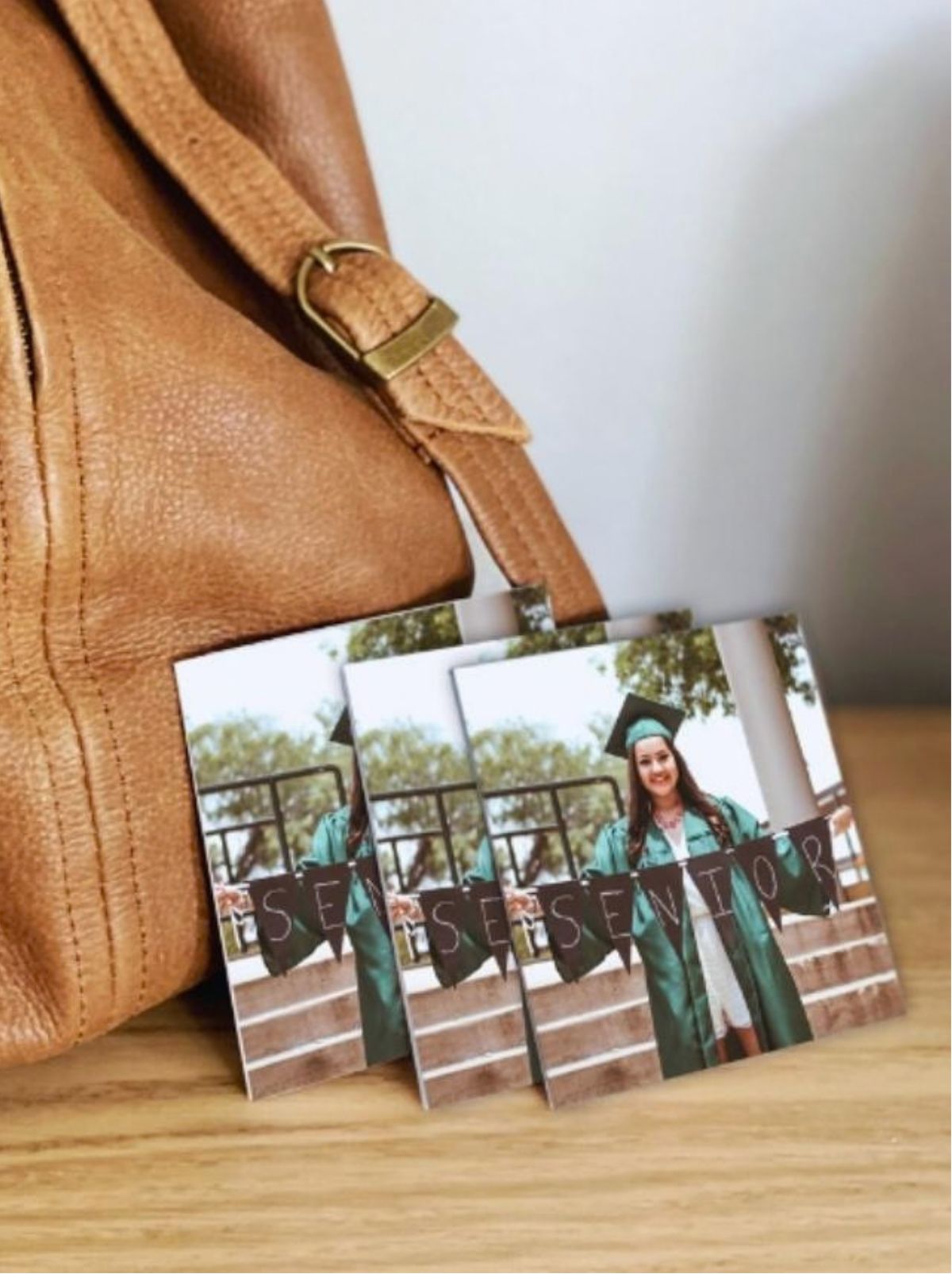 Three graduation photo cards of a smiling graduate in a green gown holding a SENIOR banner, leaning against a leather bag