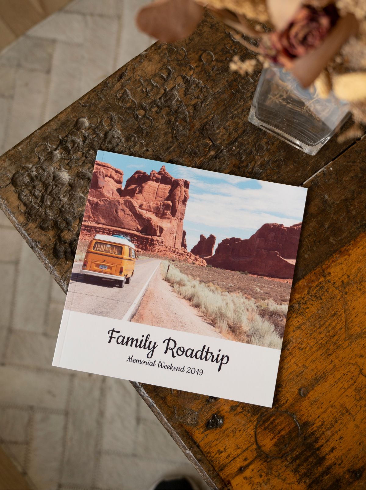 A softcover photo book titled Family Roadtrip, with an orange van on a desert road, on a wooden table