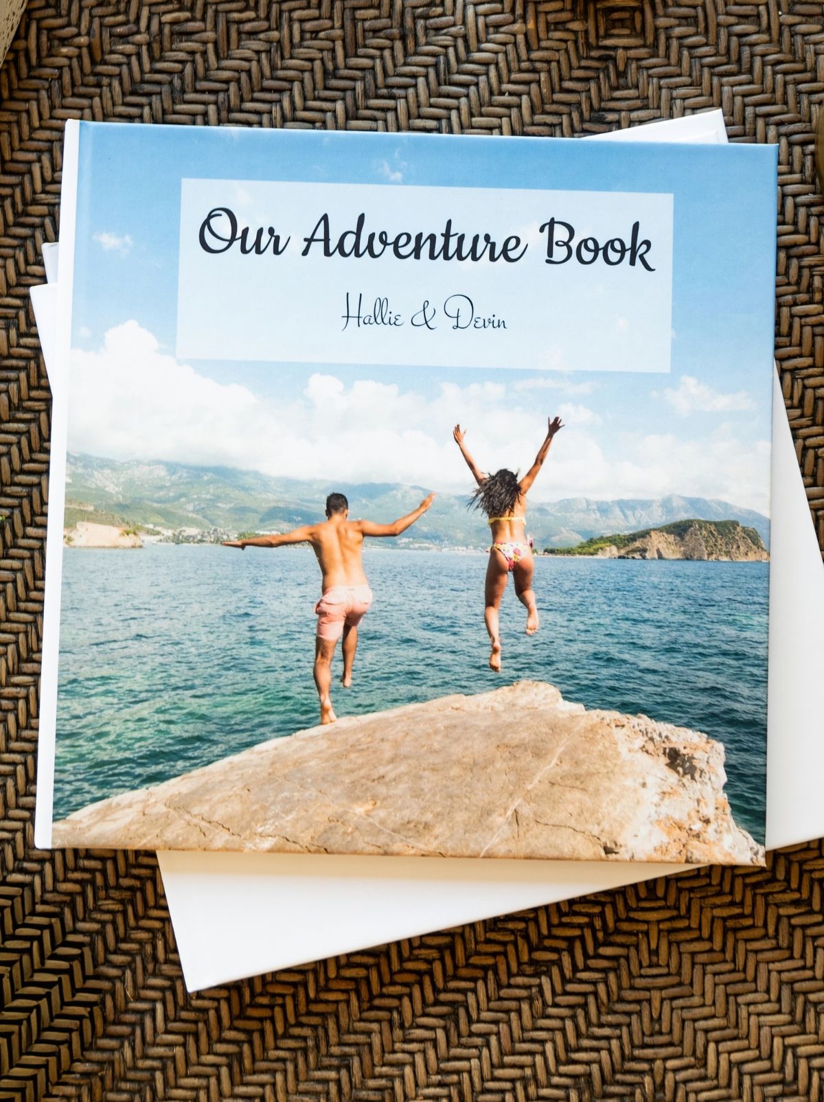 A hardcover photo book titled Our Adventure Book, with a couple jumping off a rock into the sea