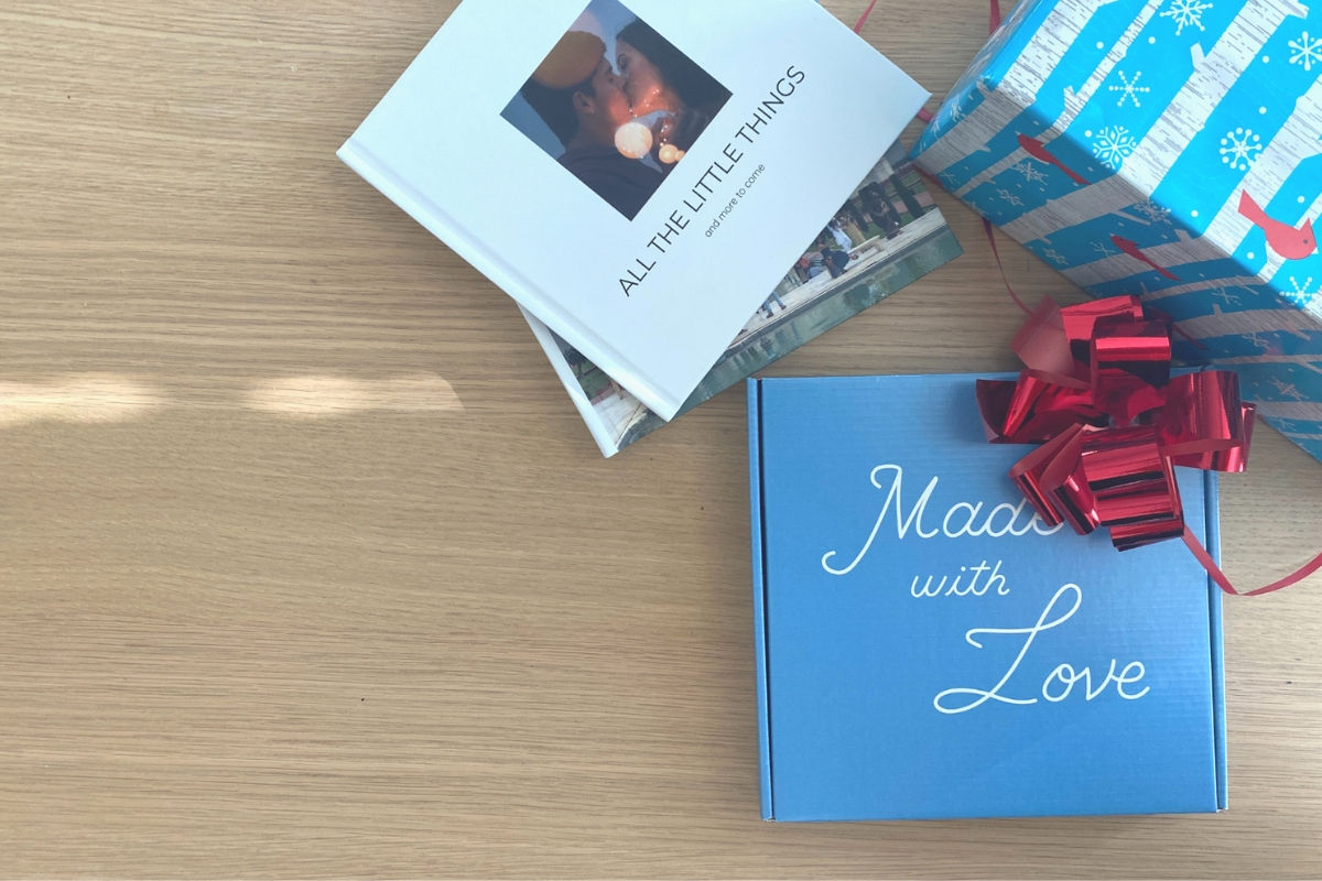 Two SimplePrints photo books next to a blue SimplePrints gift box that says Made with Love, topped with a red bow, beside a present in snowflake wrapping paper