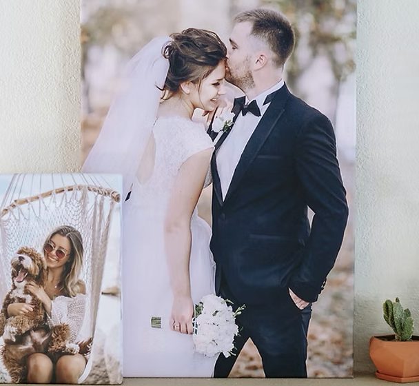 A large canvas print of a bride and groom leaning on a wall, a smaller canvas of a woman and her dog in front of it