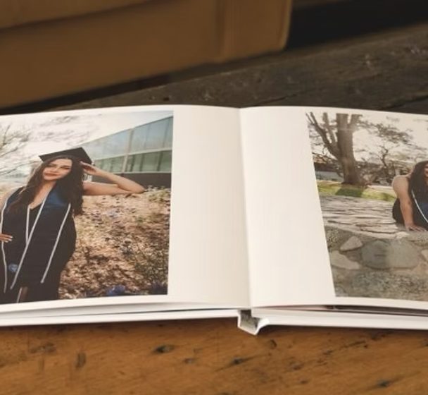 A layflat photo book lying open on a wooden table, with graduation photos on its pages