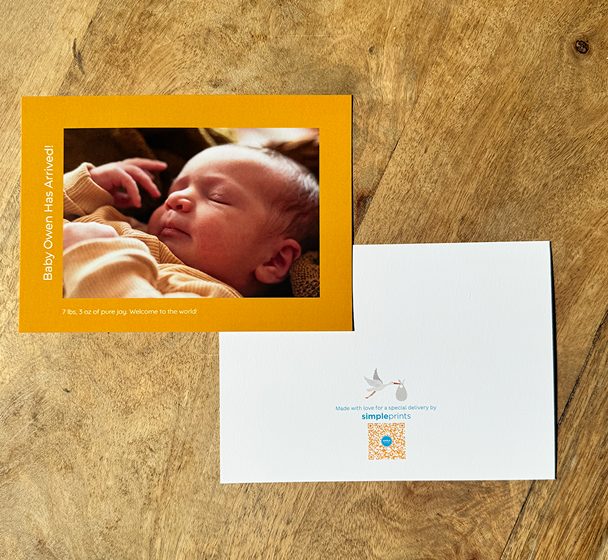 A yellow baby announcement photo card and its white back on a wooden table