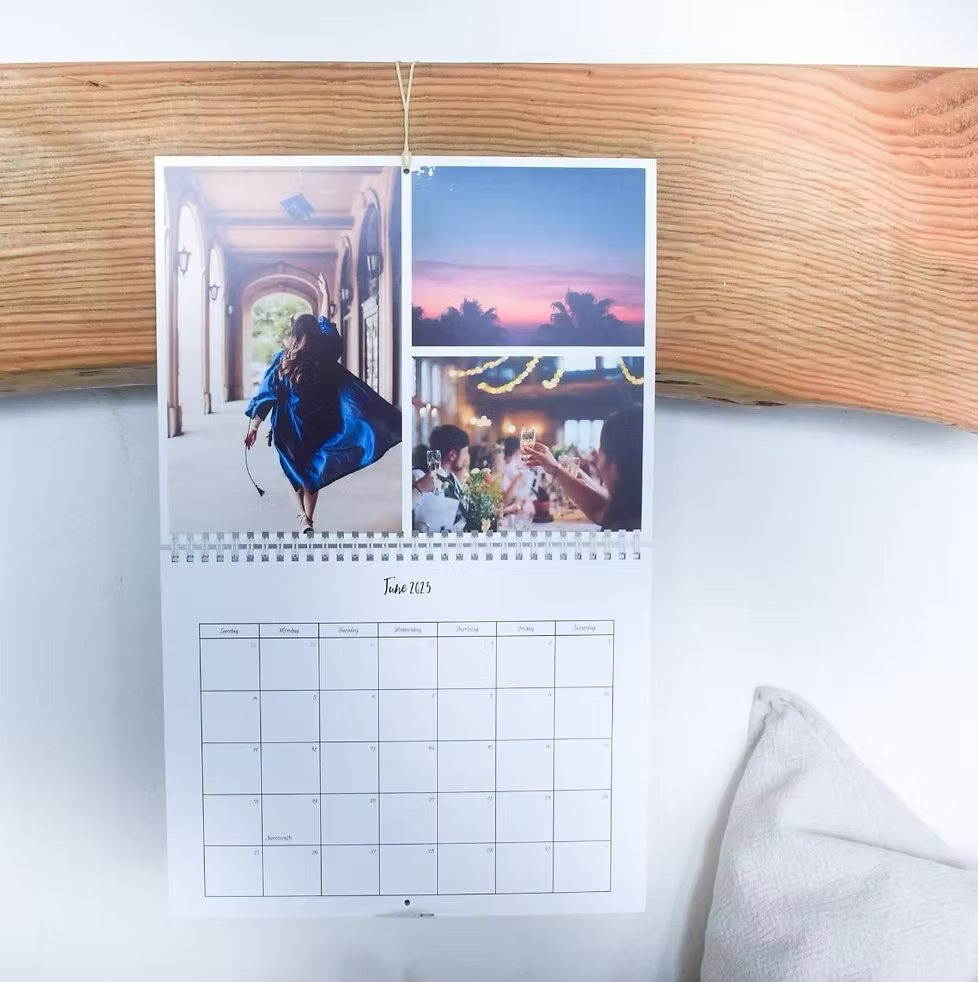 A wall calendar hanging from a wooden beam, open to June with three photos above the month